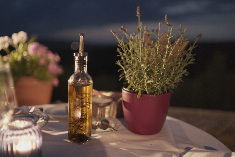 A bottle of olive oil and other items on a table at night time